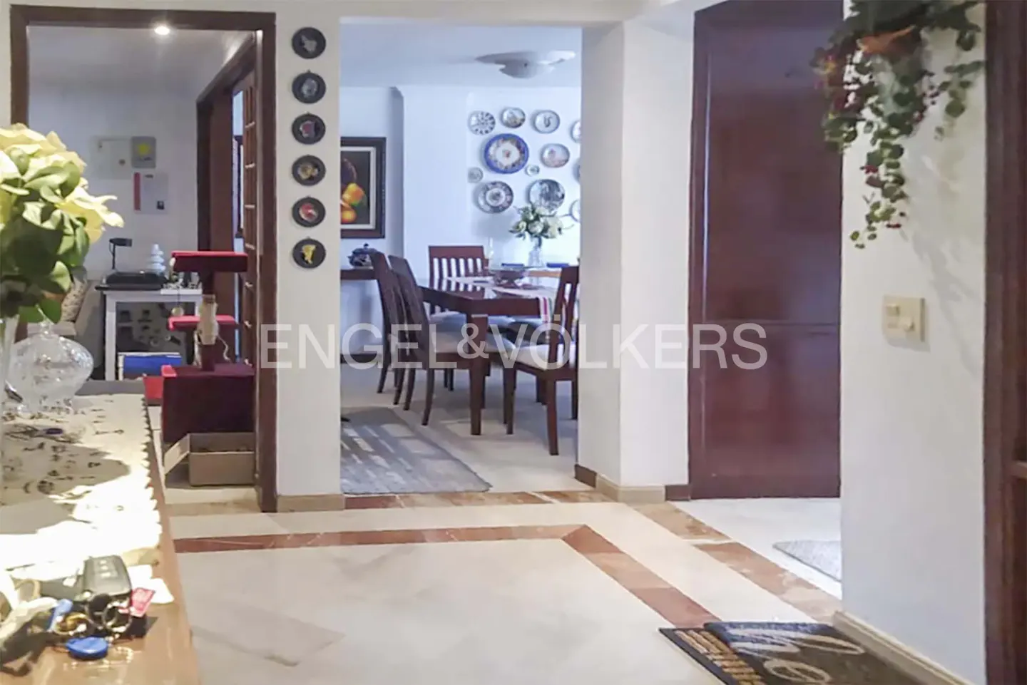 View from a hallway into a dining room with a wooden table, chairs, and decorative plates on the white walls.