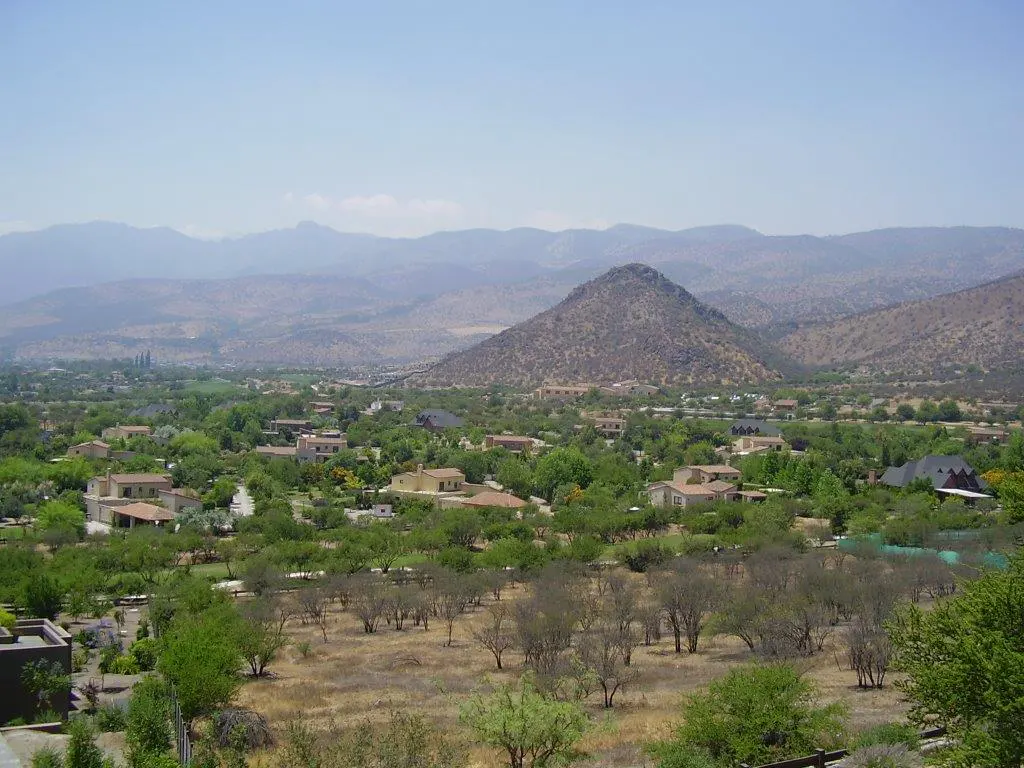 Hills and mountains overlook a valley with houses and trees under a blue sky.
