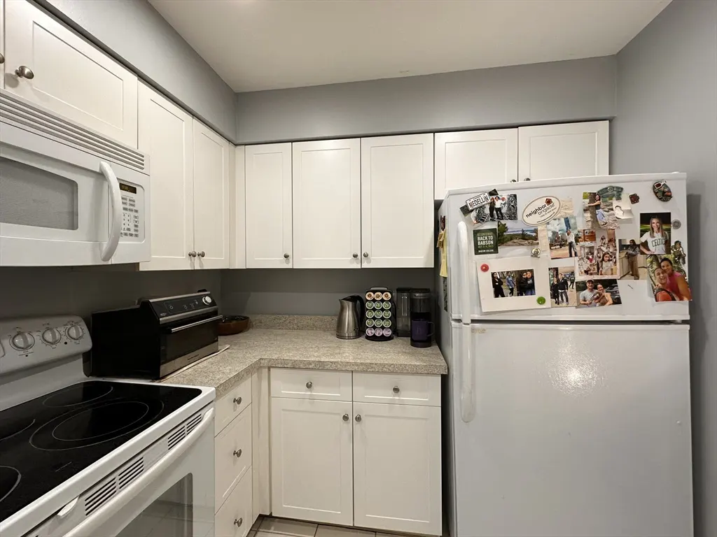 A kitchen with white cabinets, appliances, and a refrigerator covered in photos and magnets.