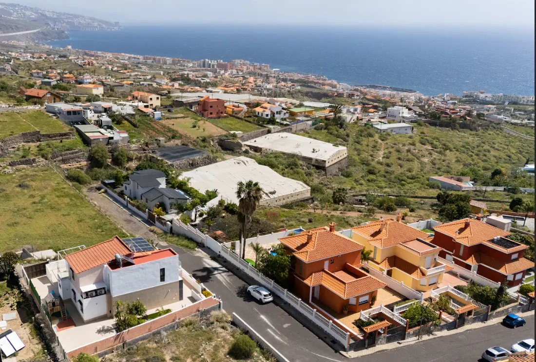 Aerial view of a neighborhood with orange-roofed houses, a white car on the road, and the ocean in the background.