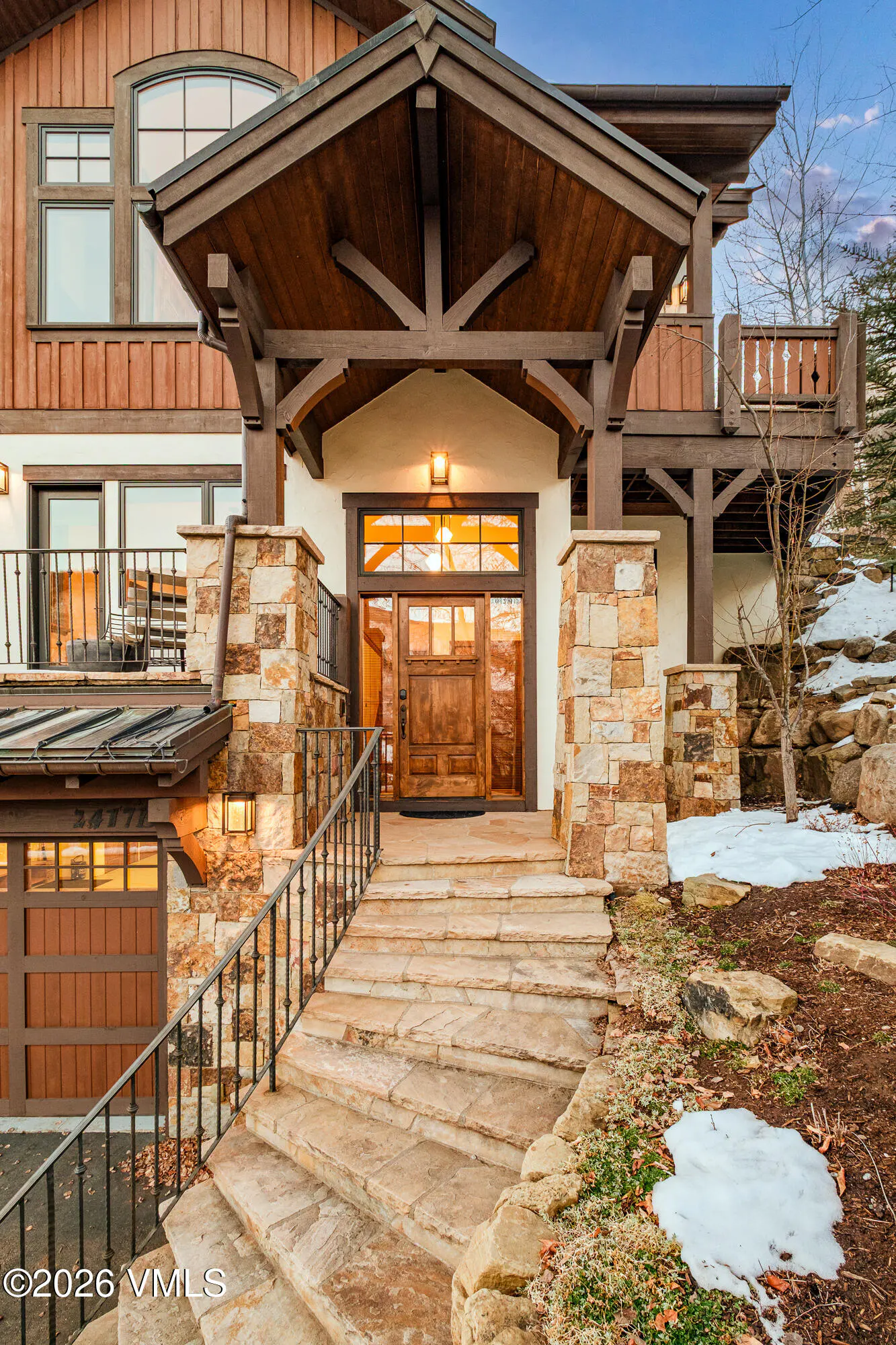 Exterior view of a luxury home with stone steps leading to a wood door and timber frame porch.