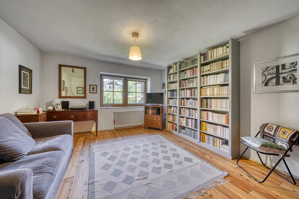 Living room with a gray sofa, a large bookshelf filled with books, and a patterned rug on a wooden floor.