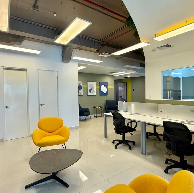 Bright office space with yellow chairs, black desks, and white walls. Abstract art hangs on the green wall in the background.