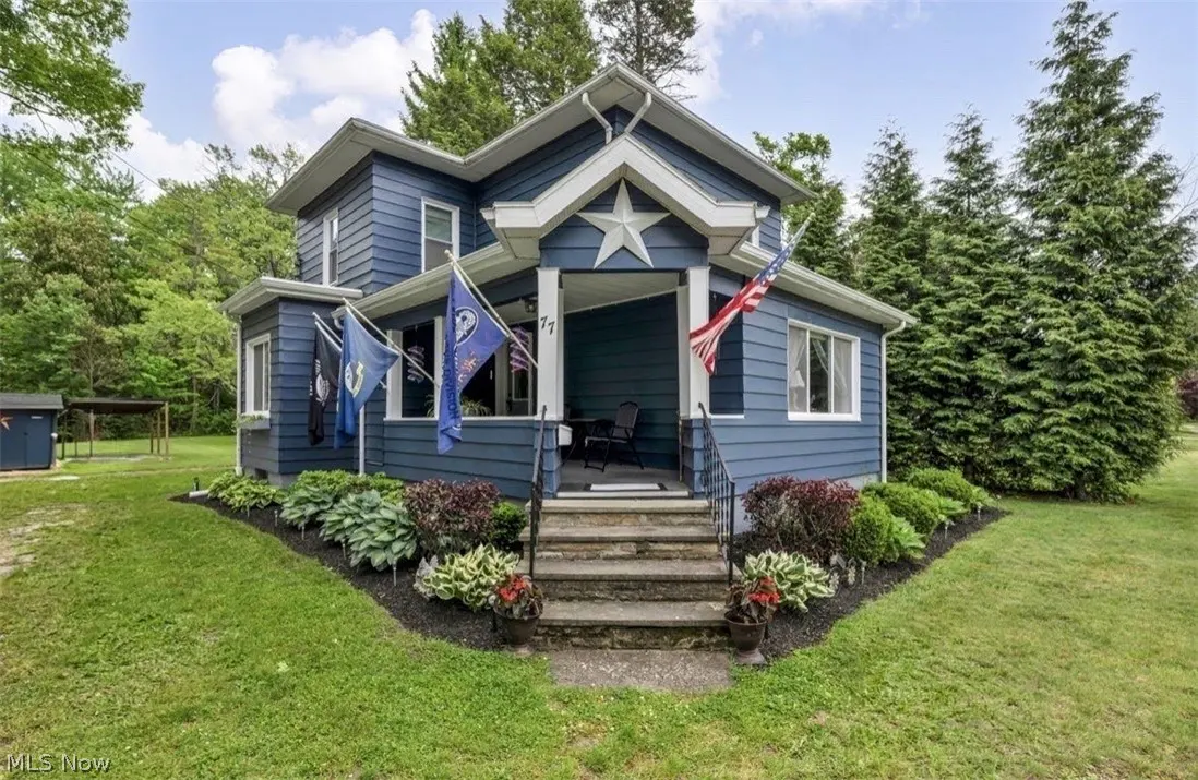 Two-story blue house with a white star on the porch, American flag, and stone steps.