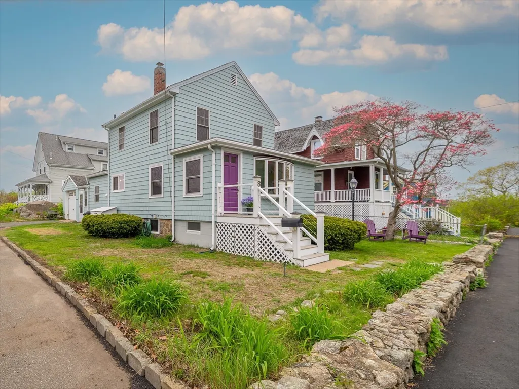 Exterior of a two-story light blue house with a purple door and white porch railing. A red house is visible in the background.
