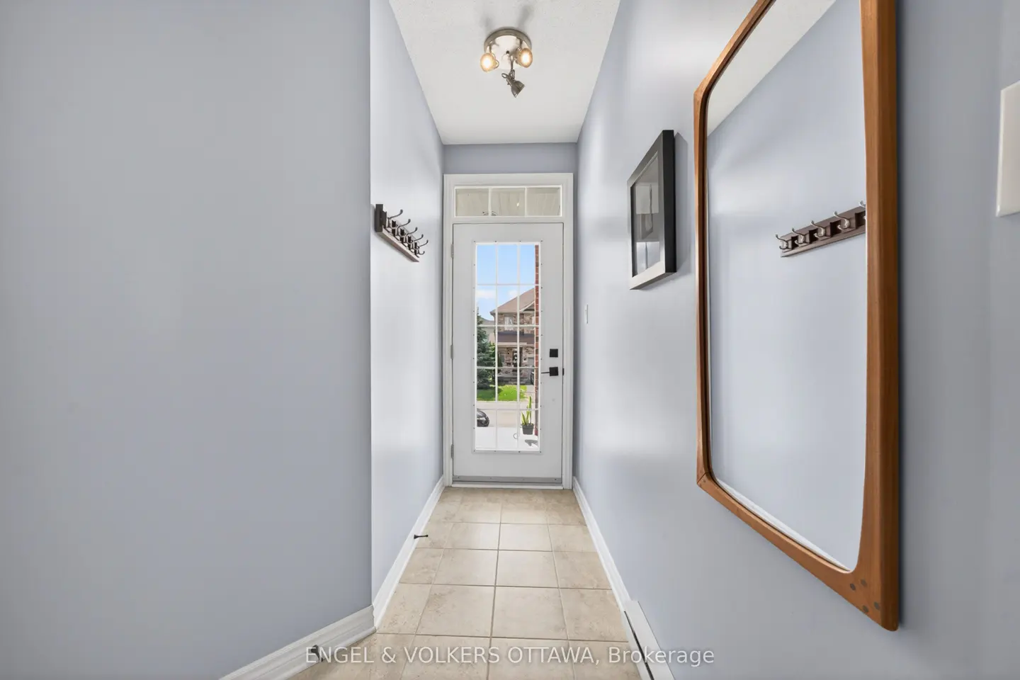 Hallway with light blue walls, beige tile floor, and a white door at the end. A wooden framed mirror hangs on the right wall.
