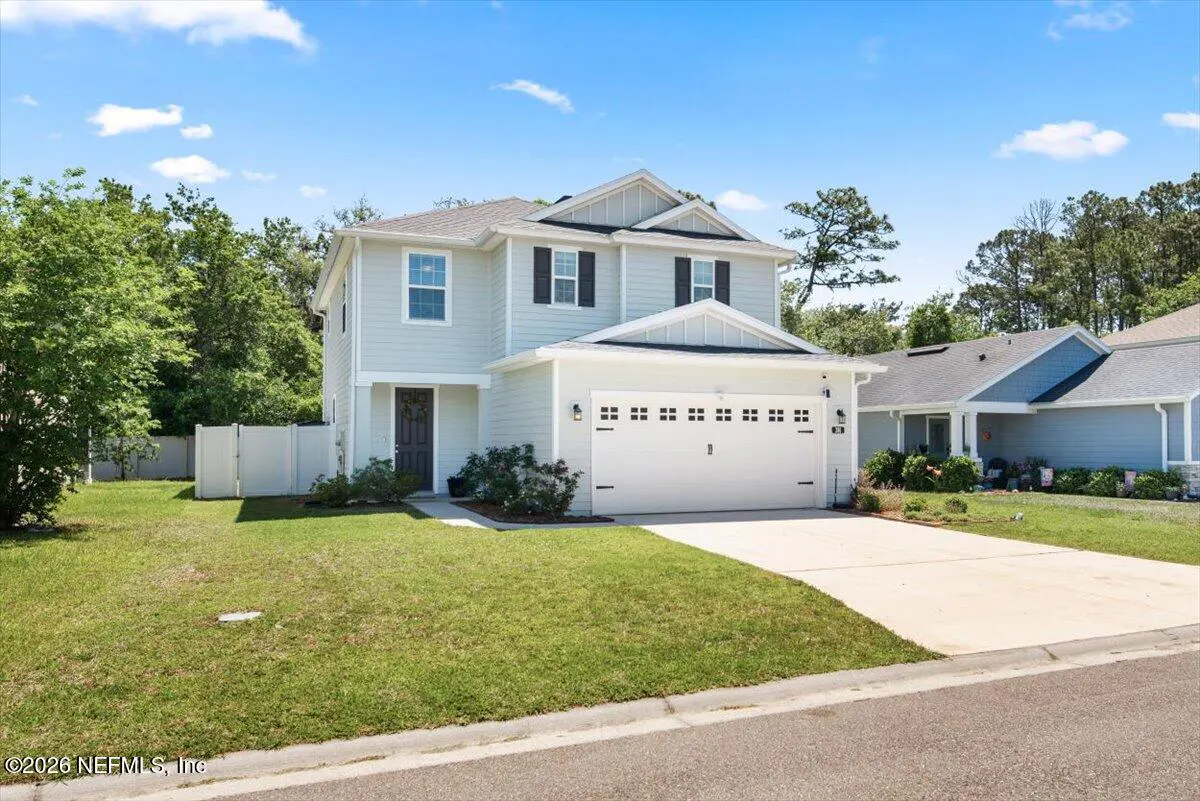 Two-story light blue house with white trim, black shutters, and a two-car garage on a sunny day.