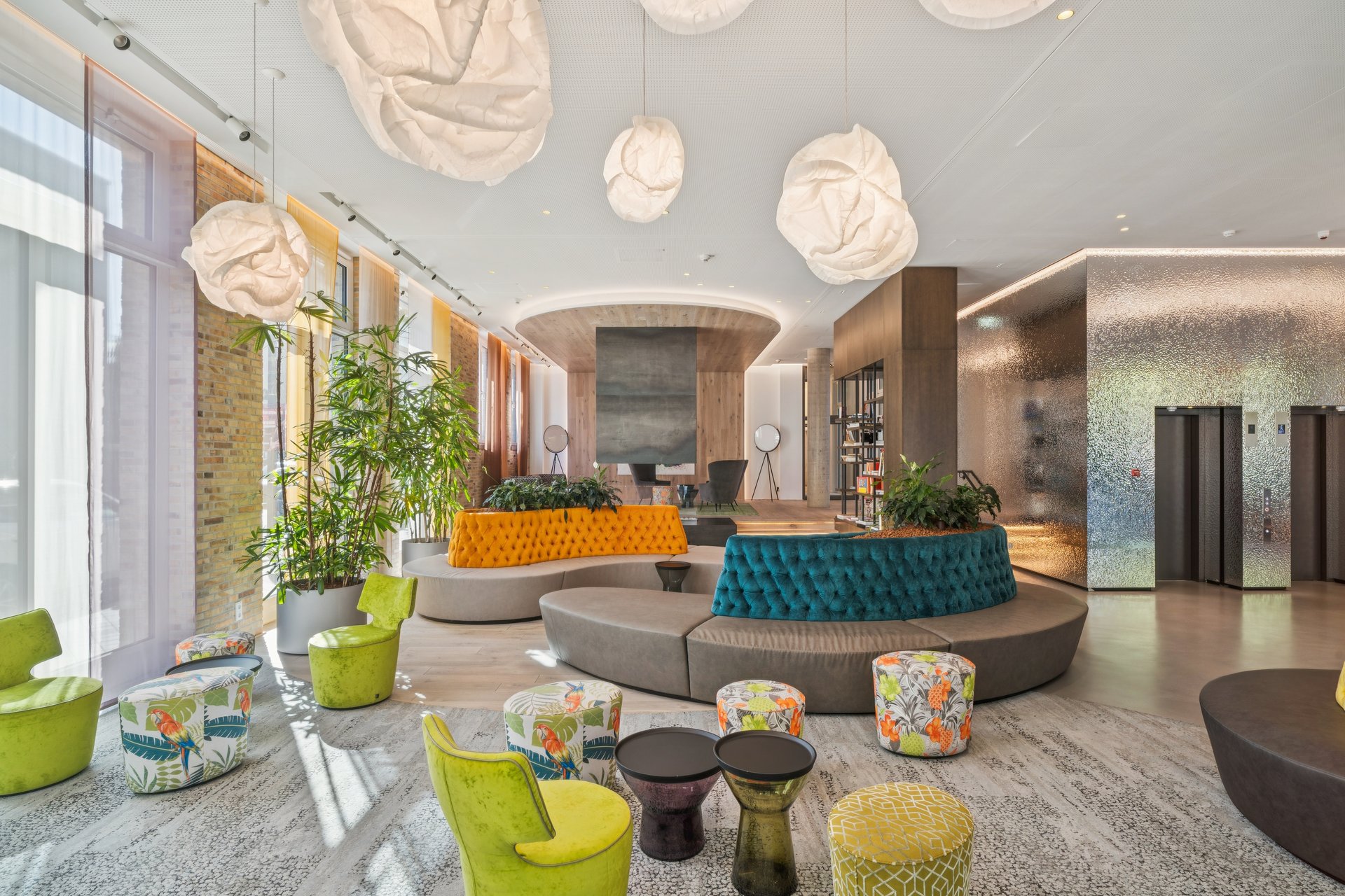 Modern hotel lobby with cloud-like pendant lights, curved orange and teal tufted sofas, and colorful patterned ottomans. [AI-generated text]
