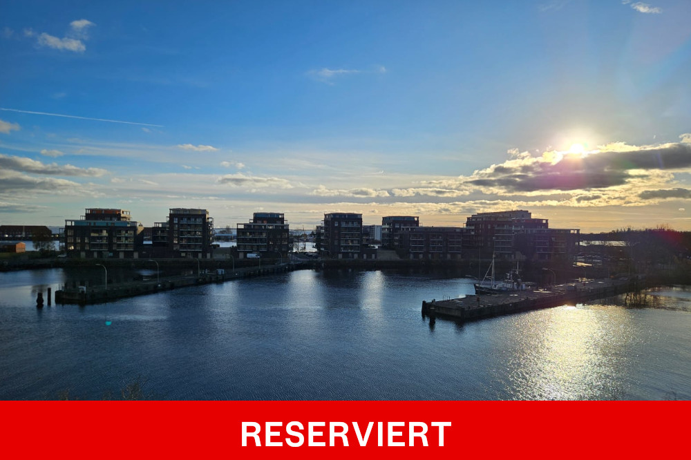 Modern apartment buildings overlooking a harbor at sunset, with a red banner at the bottom reading RESERVIERT.