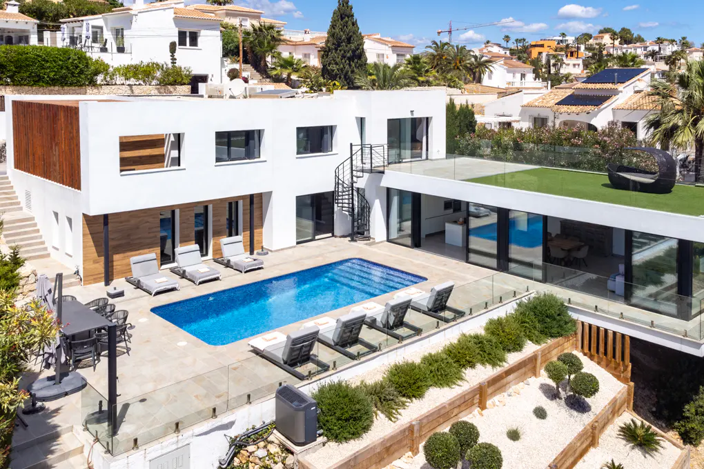 Aerial view of a modern white house with a blue pool, lounge chairs, and a rooftop terrace with green turf.
