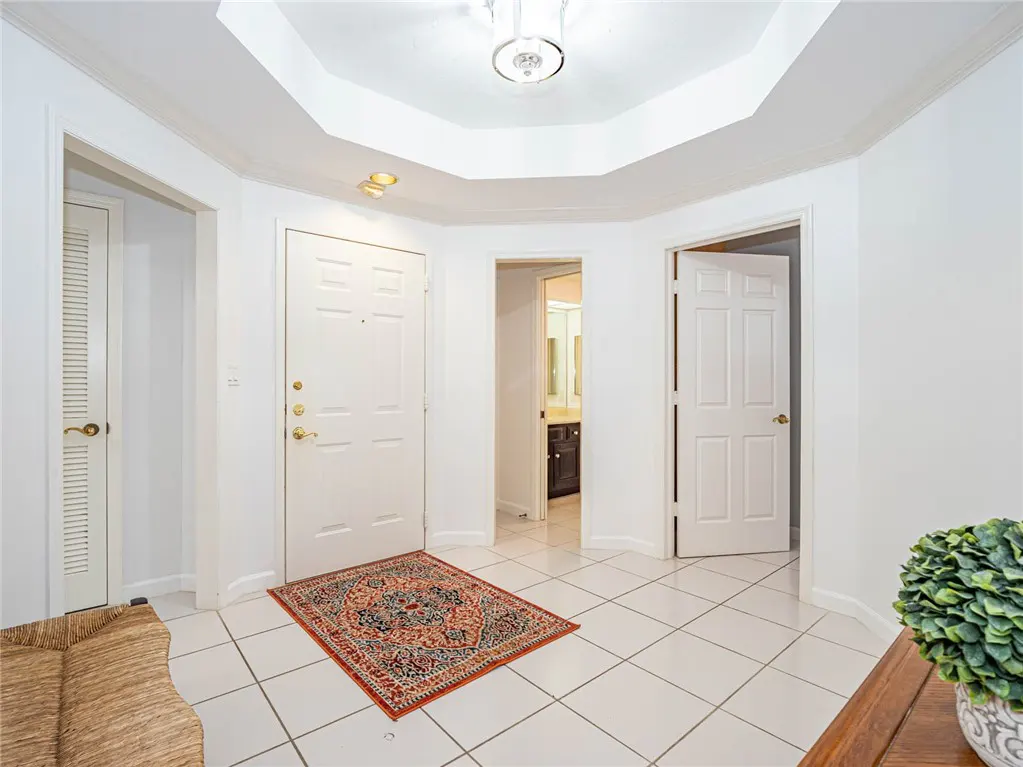 Bright foyer with white walls, tile floor, and doors. A patterned rug sits near the front door. A glimpse of a bathroom is visible.