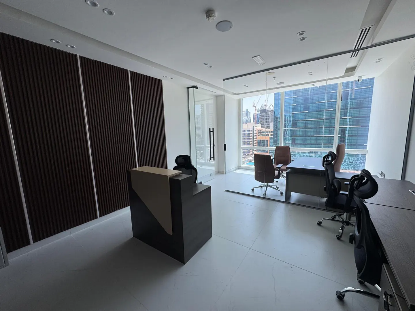 A modern office space with a reception desk, dark wood accent wall, and large windows overlooking a city skyline.