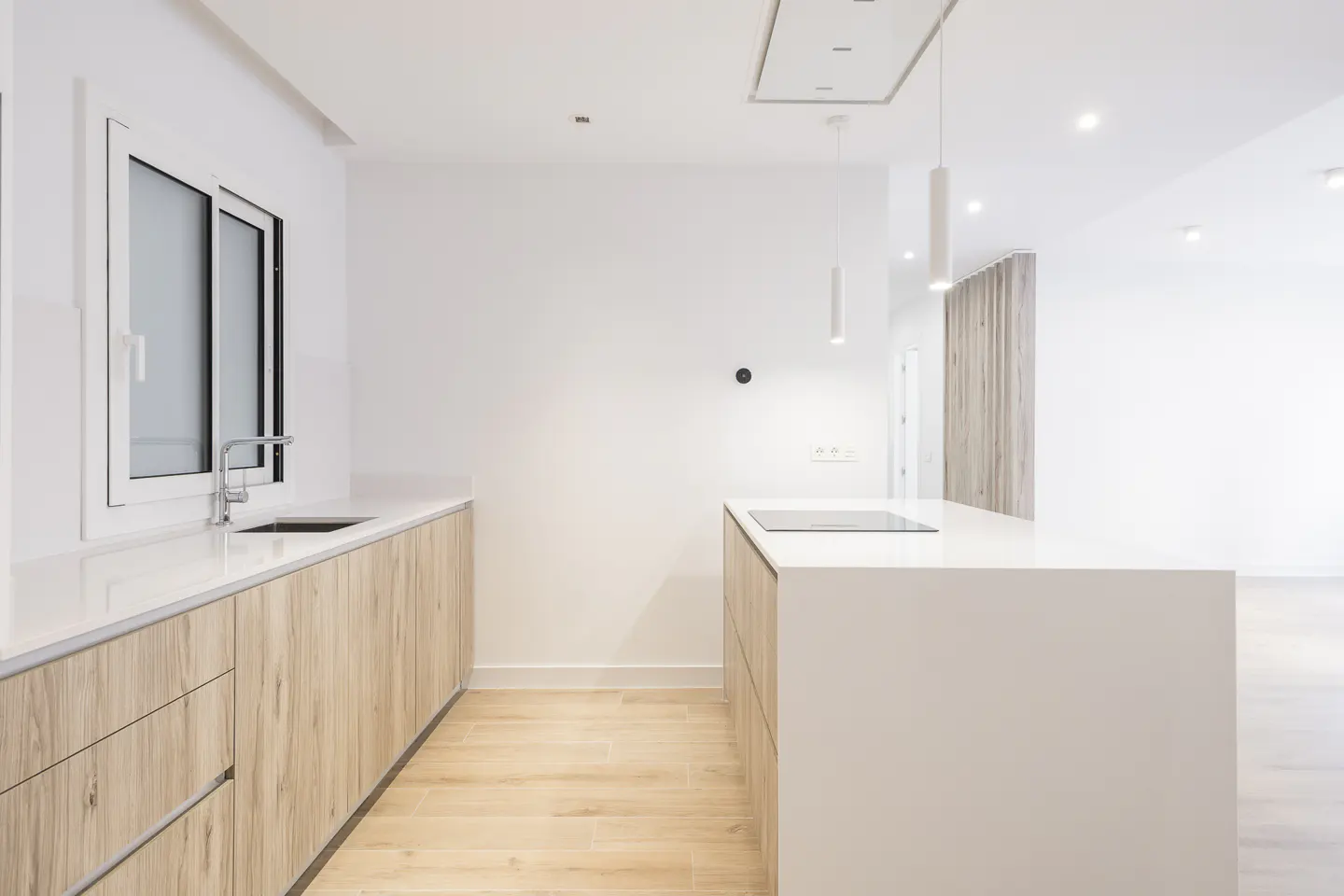Modern minimalist kitchen with light wood cabinets, white countertops, a central island, and sleek pendant lighting.