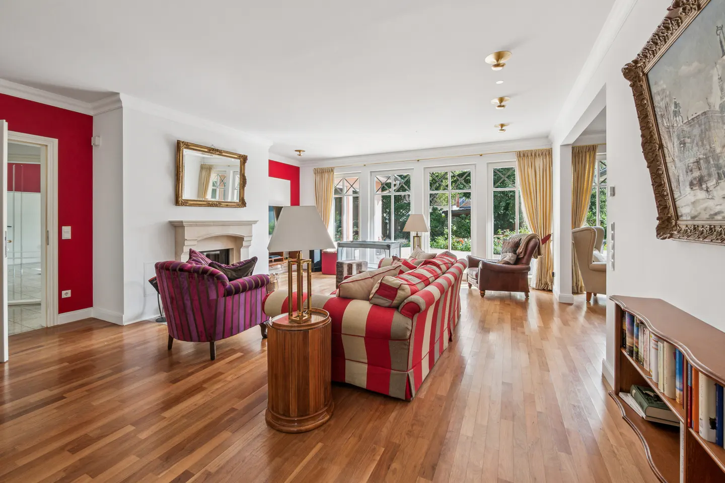 Spacious living room with hardwood floors, a red-striped sofa, purple armchair, fireplace, and large windows with curtains.
