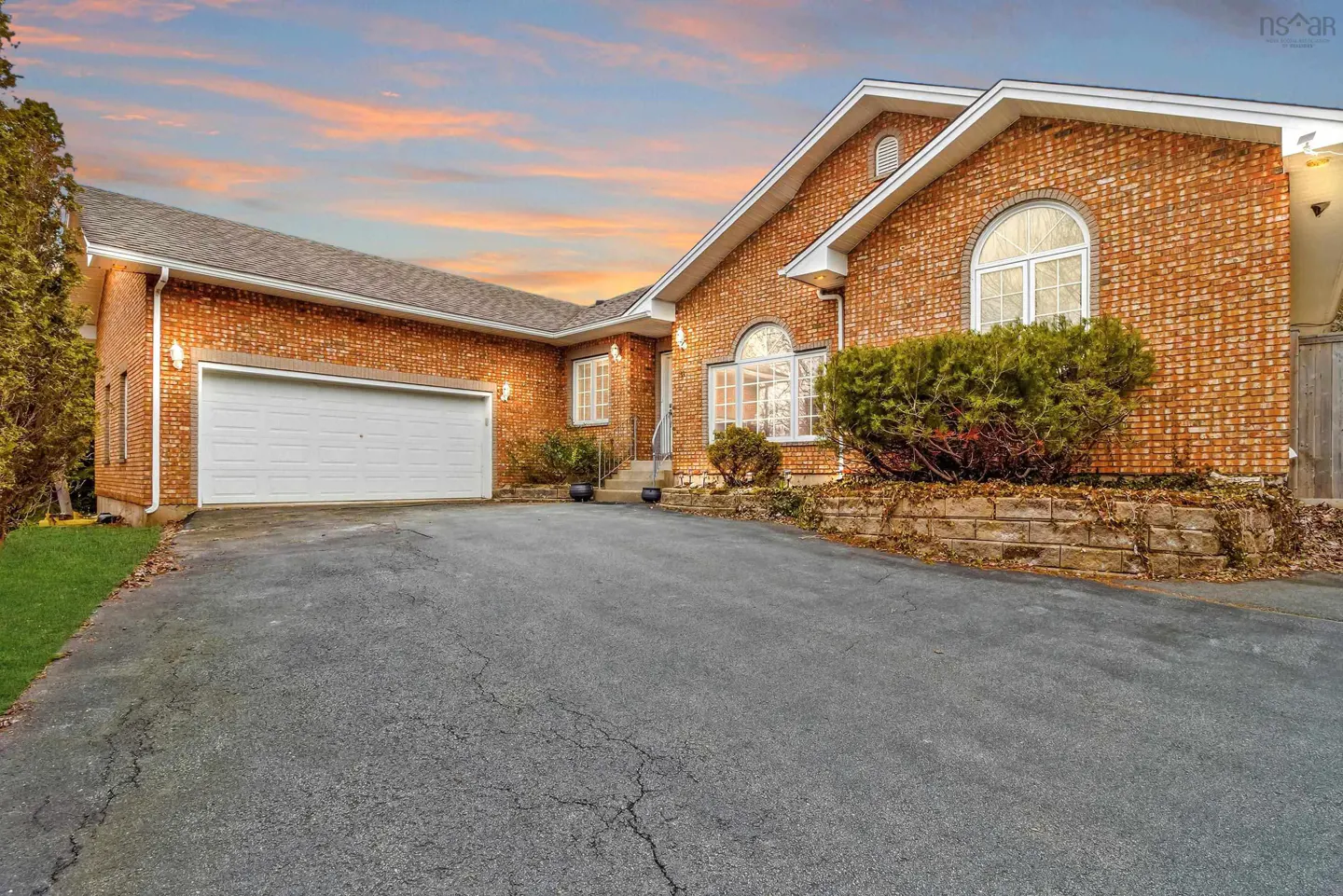 Brick house with a white garage door and arched windows, set against a colorful sunset sky.