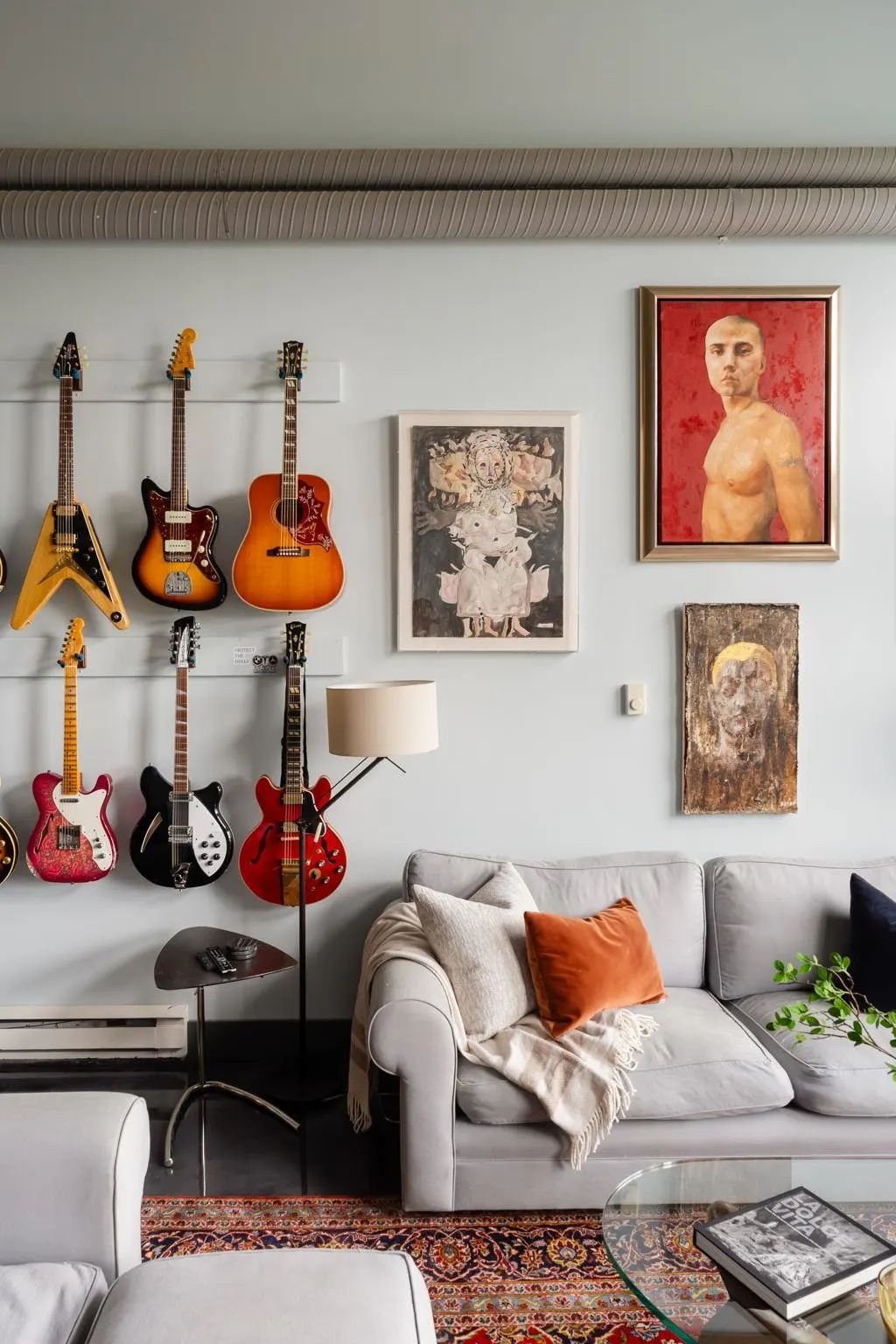 Living room with guitars mounted on the wall above a gray sofa with colorful pillows and artwork.