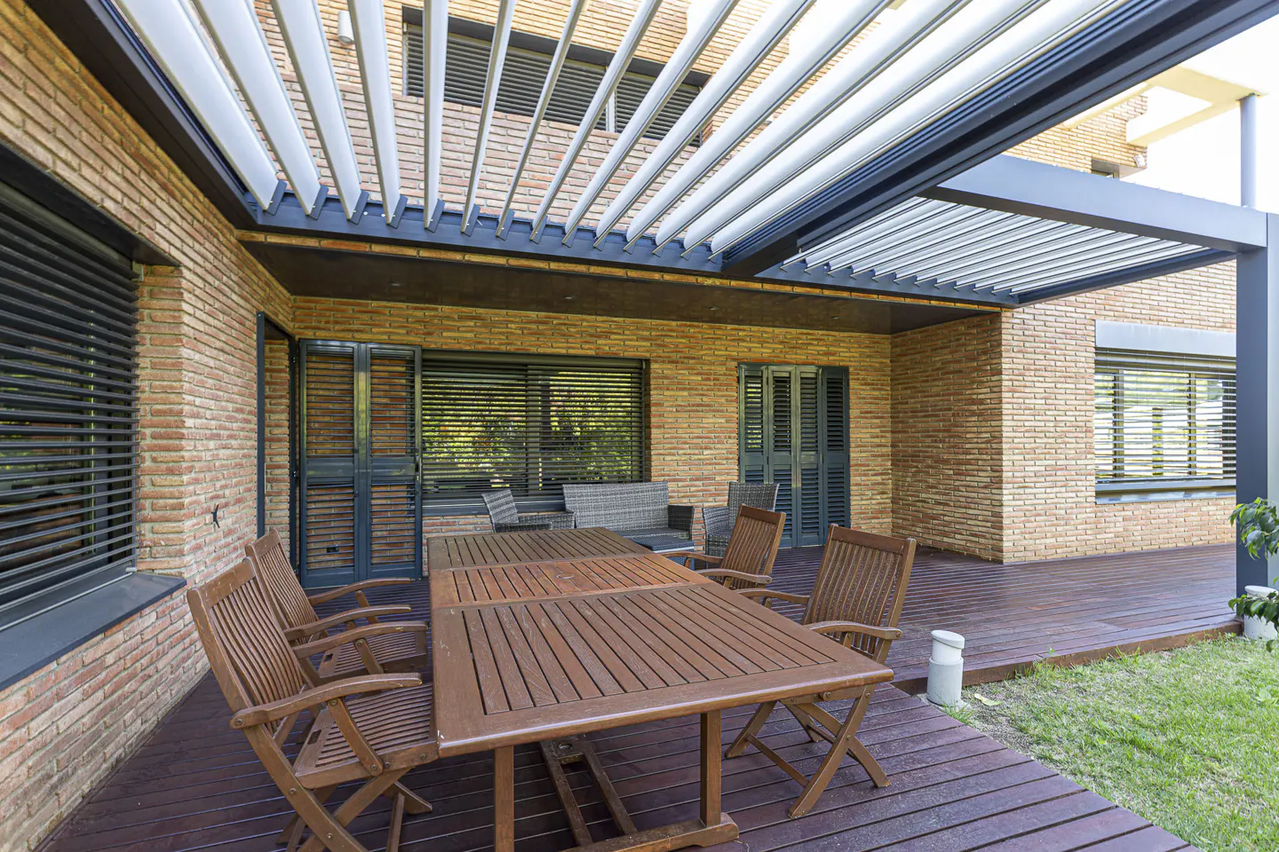 Outdoor patio with a wooden table and chairs on a wooden deck, brick walls, and a modern pergola.