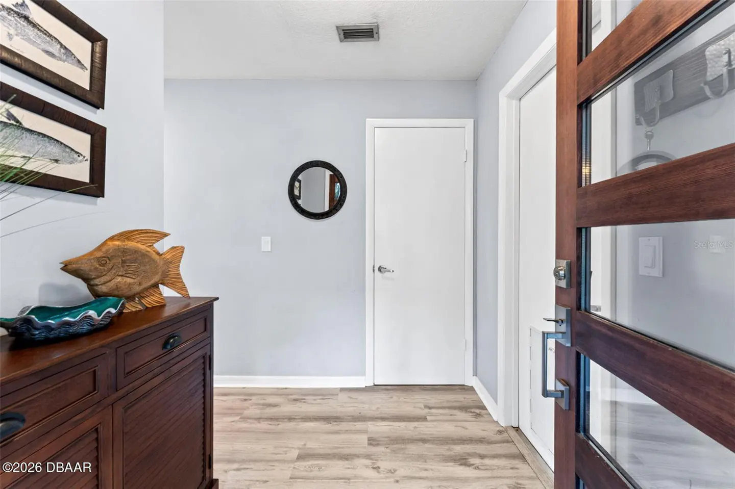 Entryway with light blue walls, wood floors, and a dark wood cabinet with fish decor. A modern wood and glass door is ajar.