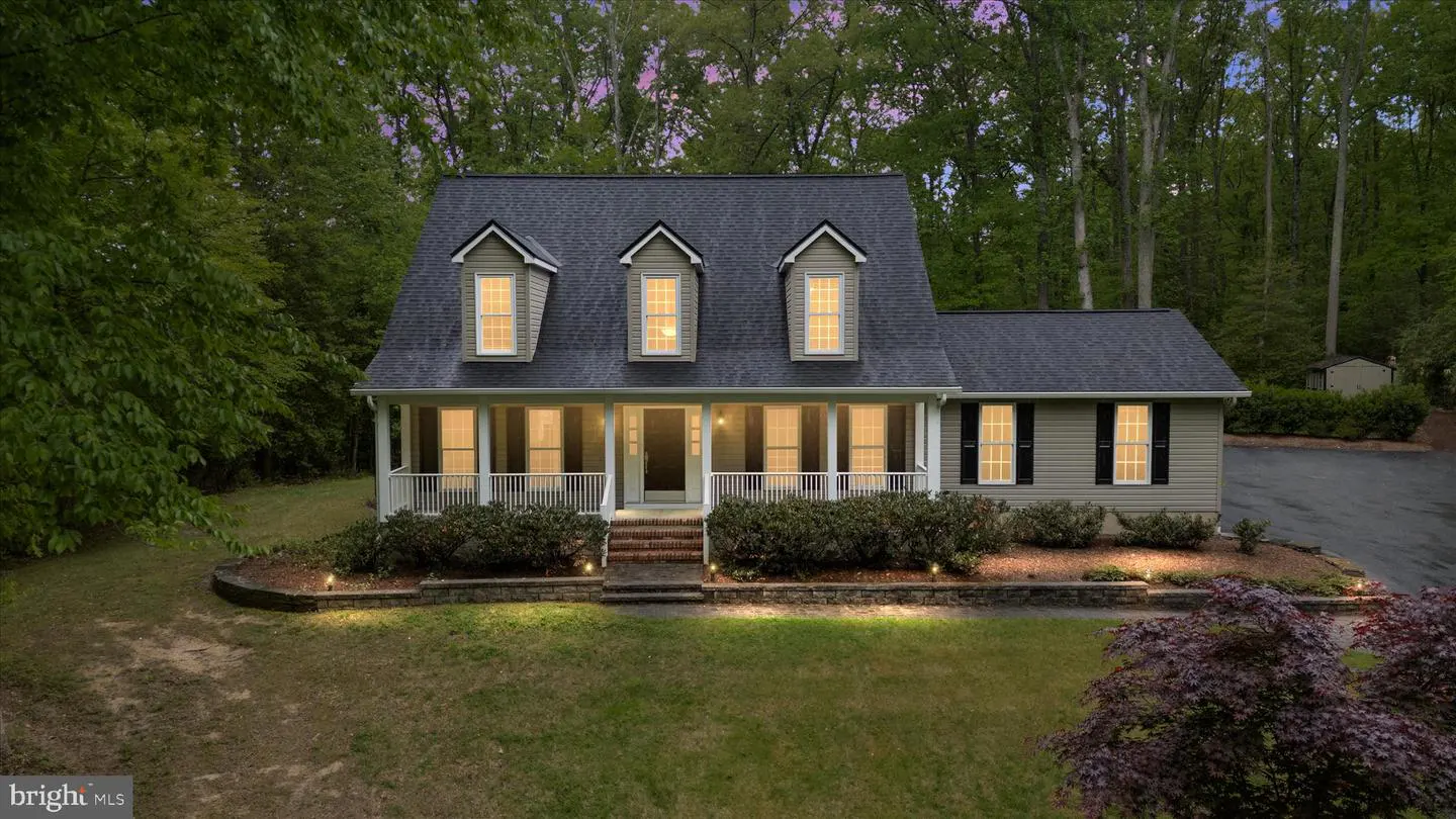A two-story house with a gray roof, light green siding, and a white porch is surrounded by trees.