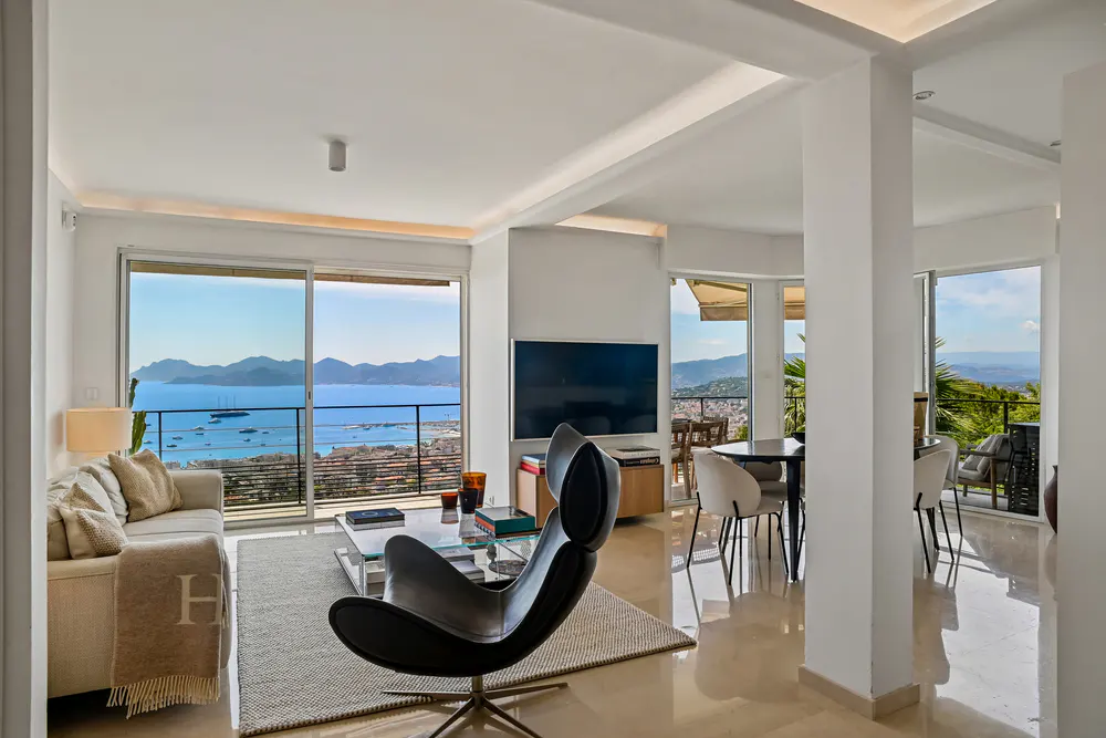 Bright, modern living room with a black chair, white sofa, and a view of the ocean through large windows.