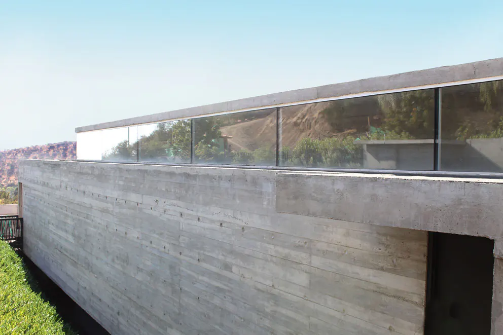 Exterior view of a modern concrete house with large windows reflecting the surrounding landscape.