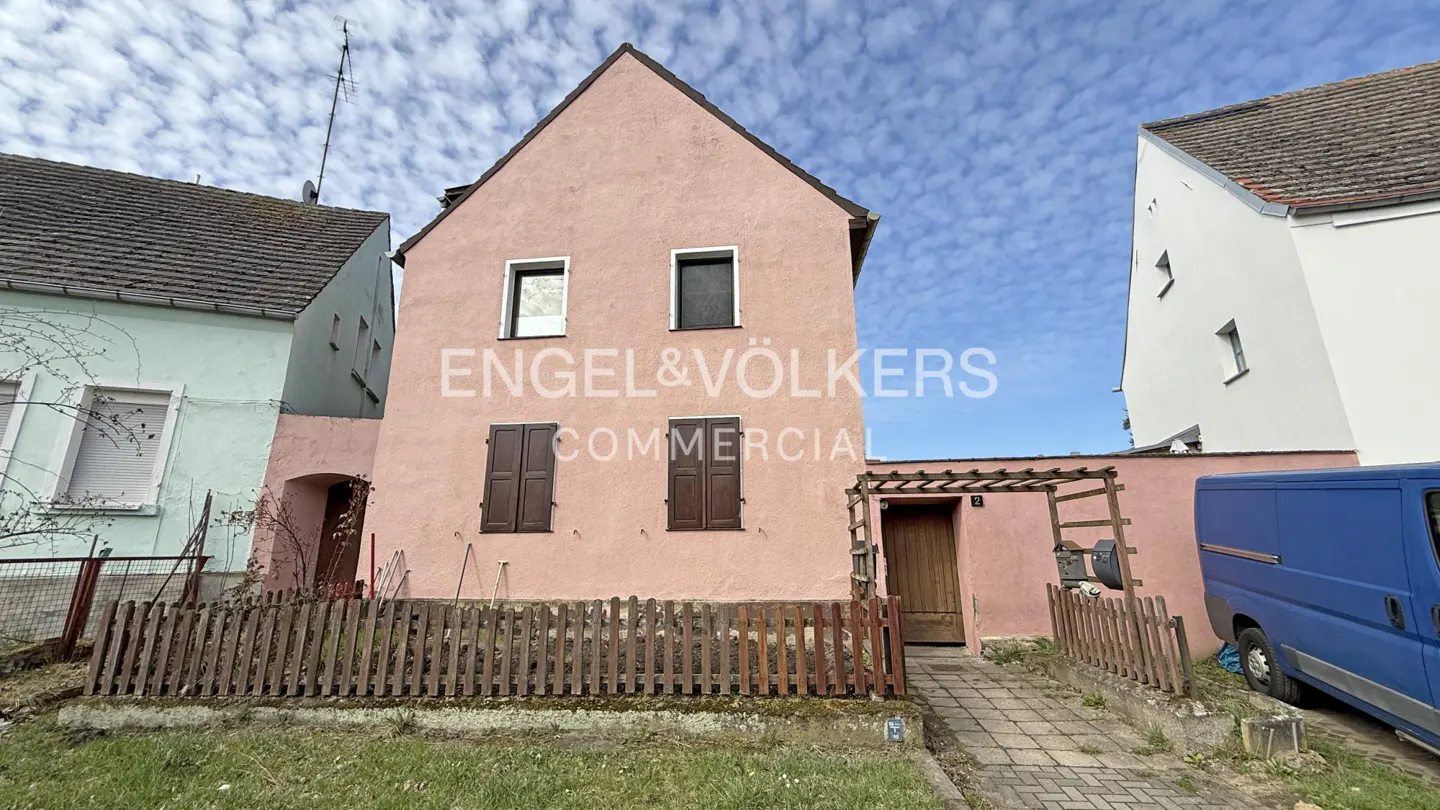 Exterior view of a two-story pink building with brown shutters, a wooden fence, and an Engel & Völkers sign.