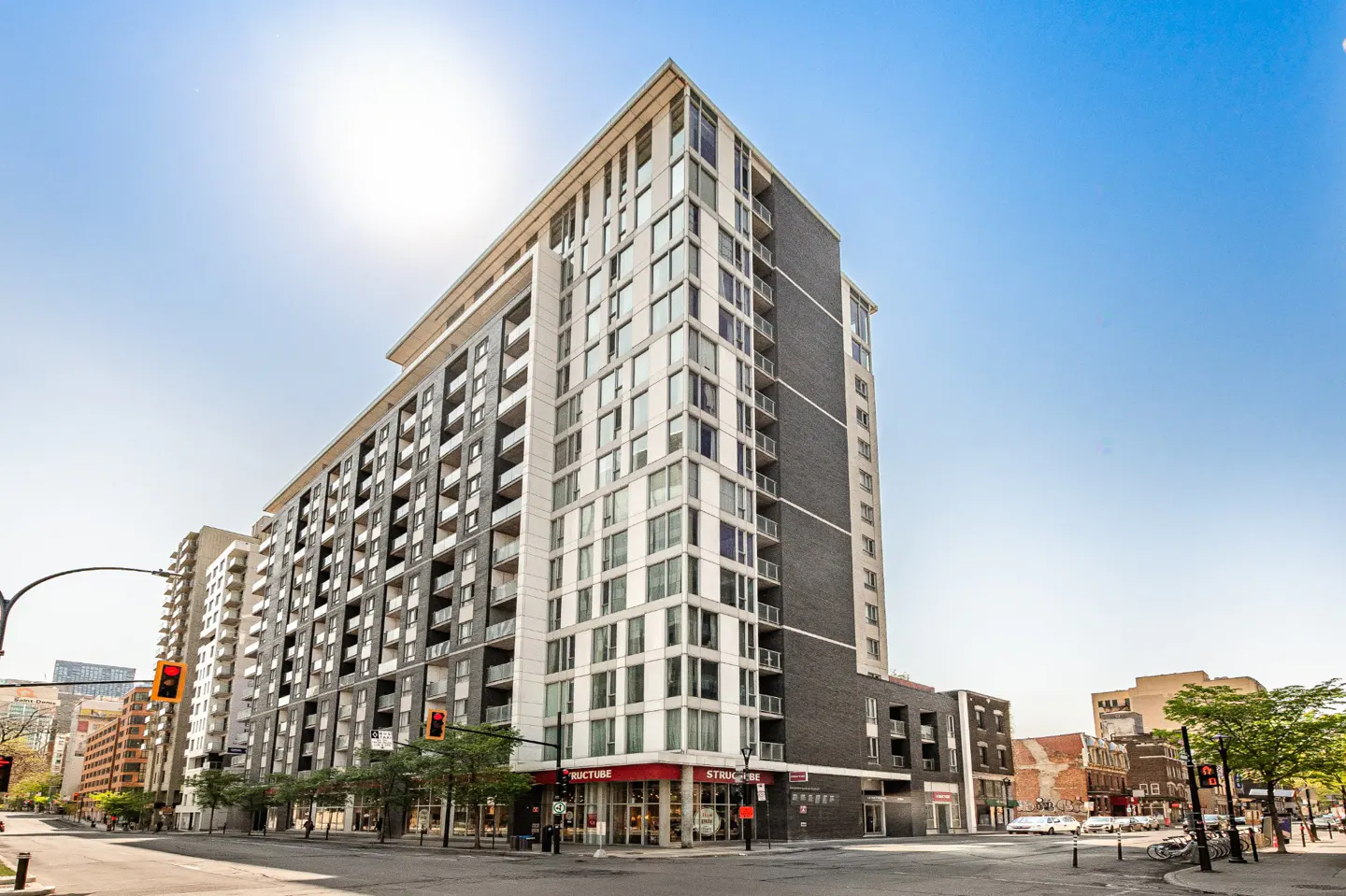 Modern high-rise apartment building with gray brick and white balconies on a city street.