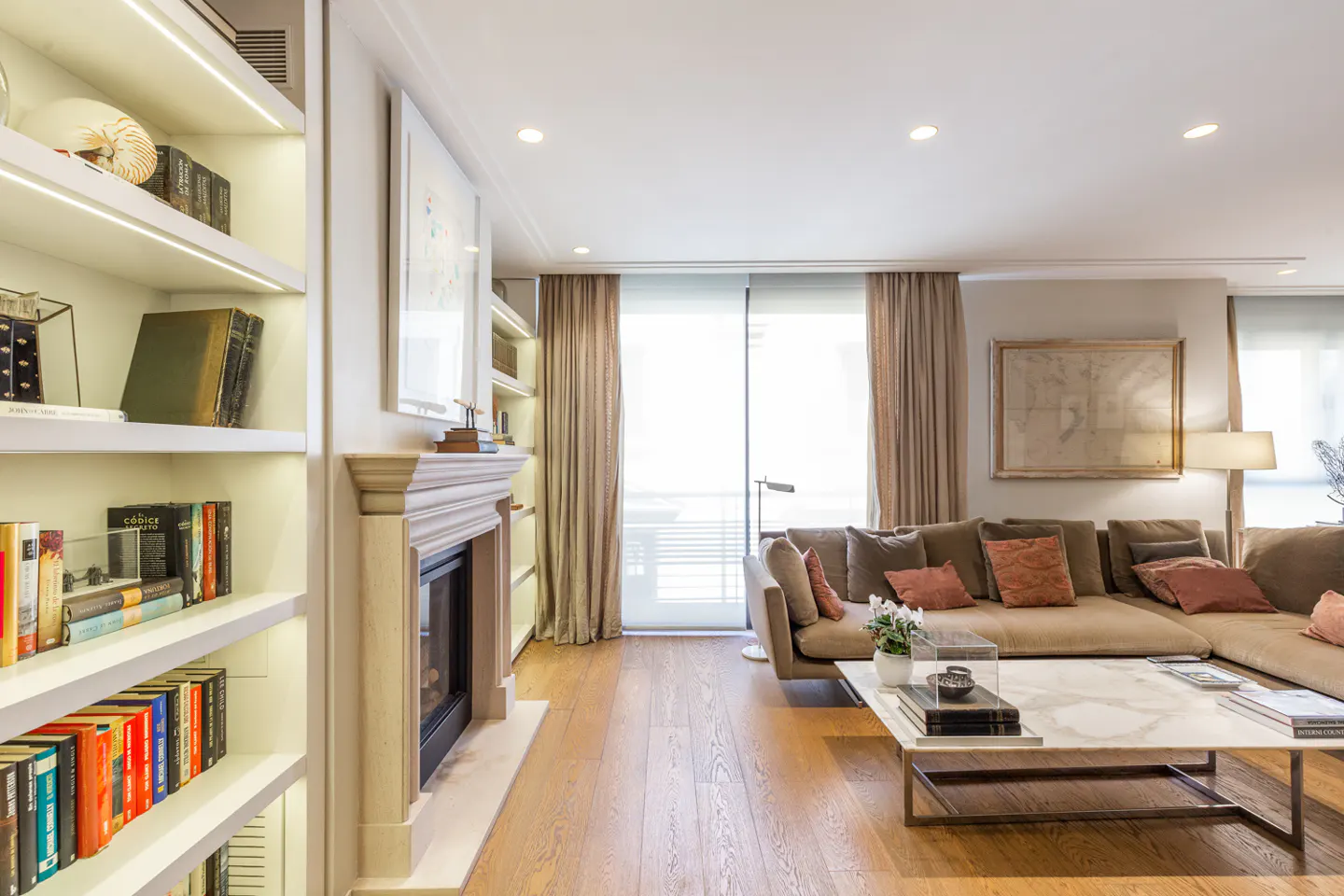 Bright living room with hardwood floors, a beige sectional sofa, and a marble coffee table. A fireplace and built-in bookshelves add character.