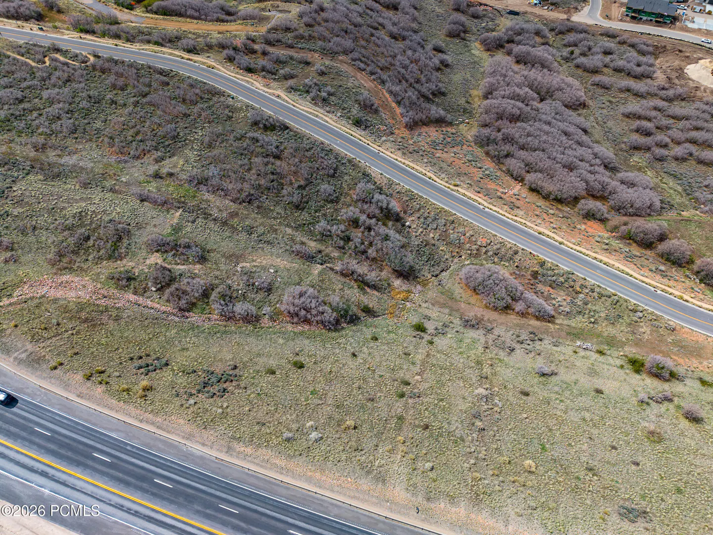 Aerial view of a grassy hillside with roads, shrubs, and some trees.