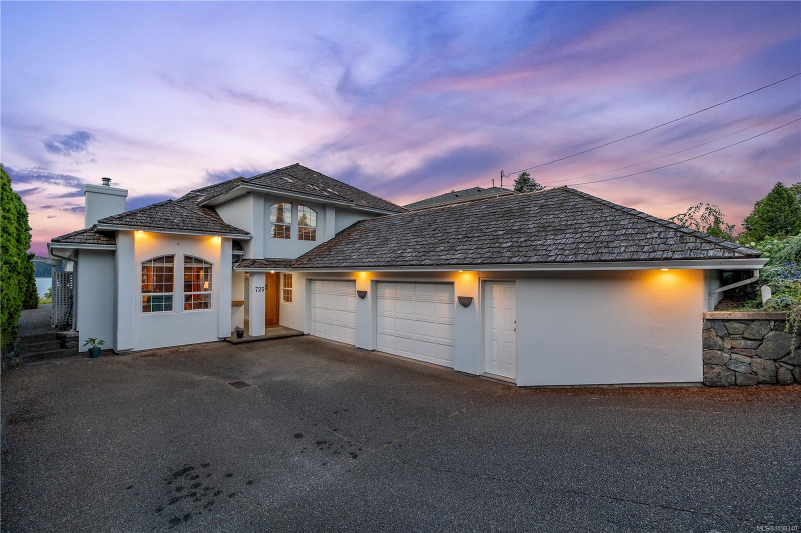 Exterior shot of a two-story white house with a gray roof and three-car garage at dusk.