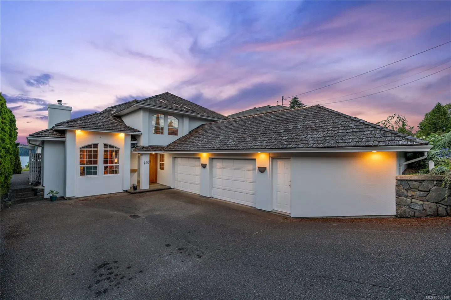 Exterior shot of a two-story white house with a gray roof and three-car garage at dusk.