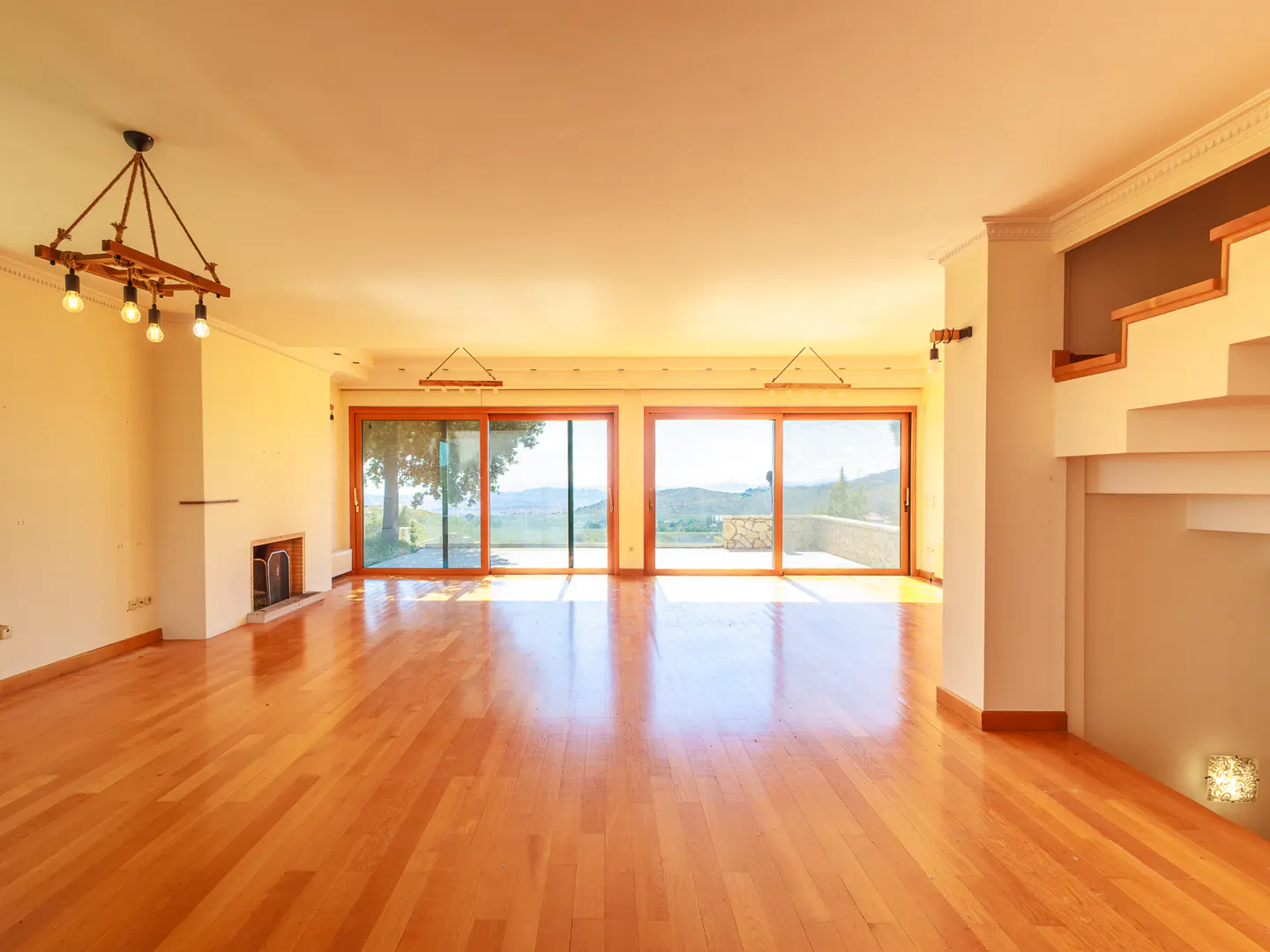 Bright, empty living room with hardwood floors, fireplace, and sliding glass doors to a patio with a view.