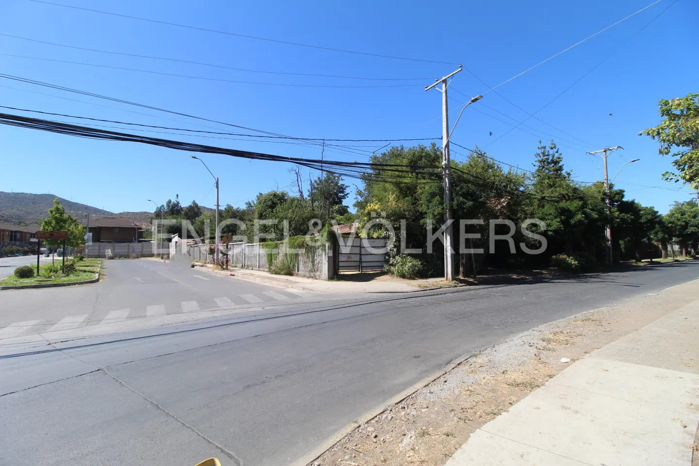 Street view of a property with a white fence and gate, surrounded by trees under a clear blue sky.