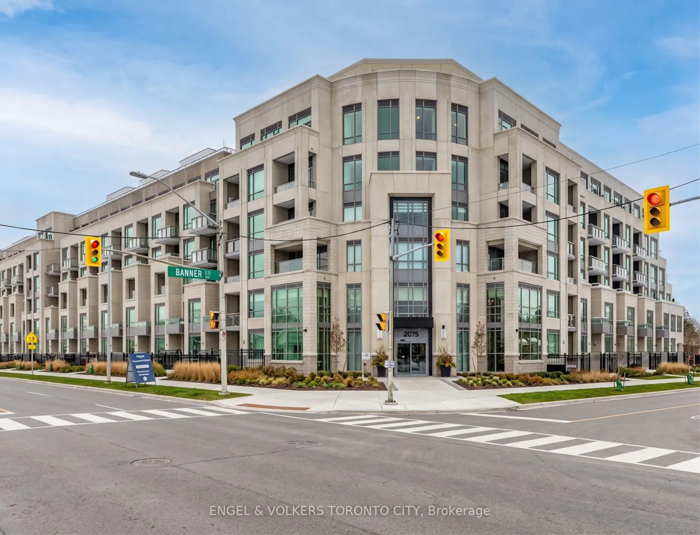 Exterior view of a modern, light-beige condo building with balconies and large windows, located at a street corner with traffic lights.
