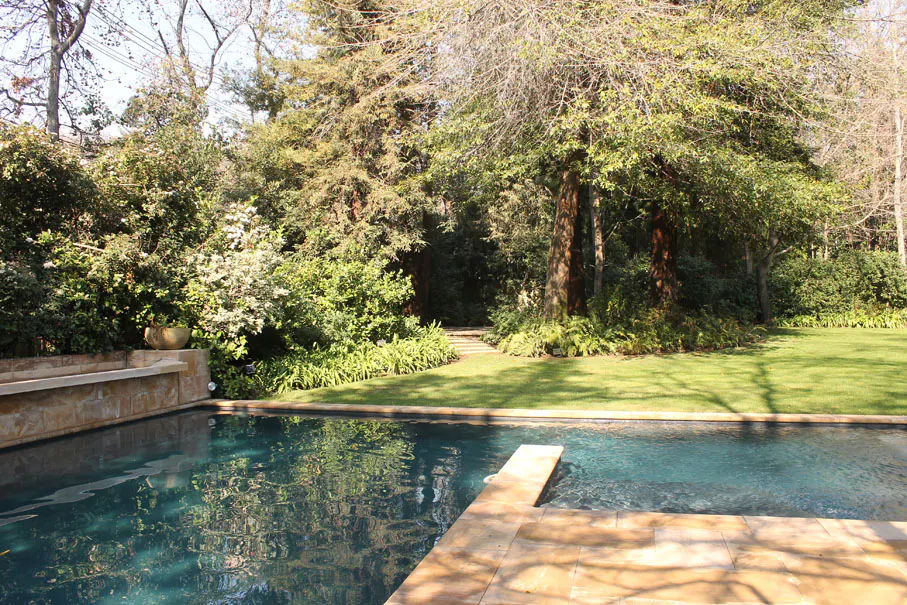 A backyard pool with a diving board, surrounded by green grass and trees.