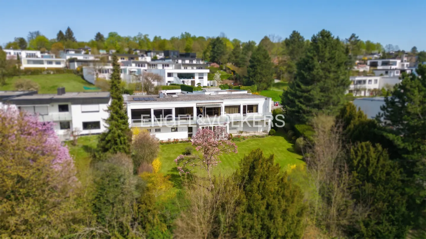 Aerial view of a modern white house with a green lawn and trees under a blue sky.