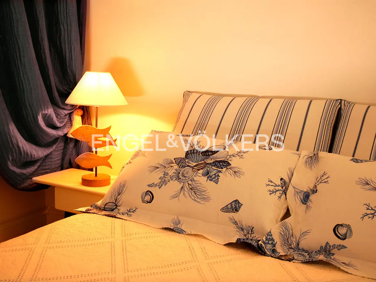 Bedroom with a lamp featuring wooden fish, blue seashell-patterned pillows, and dark blue curtains in warm lighting.