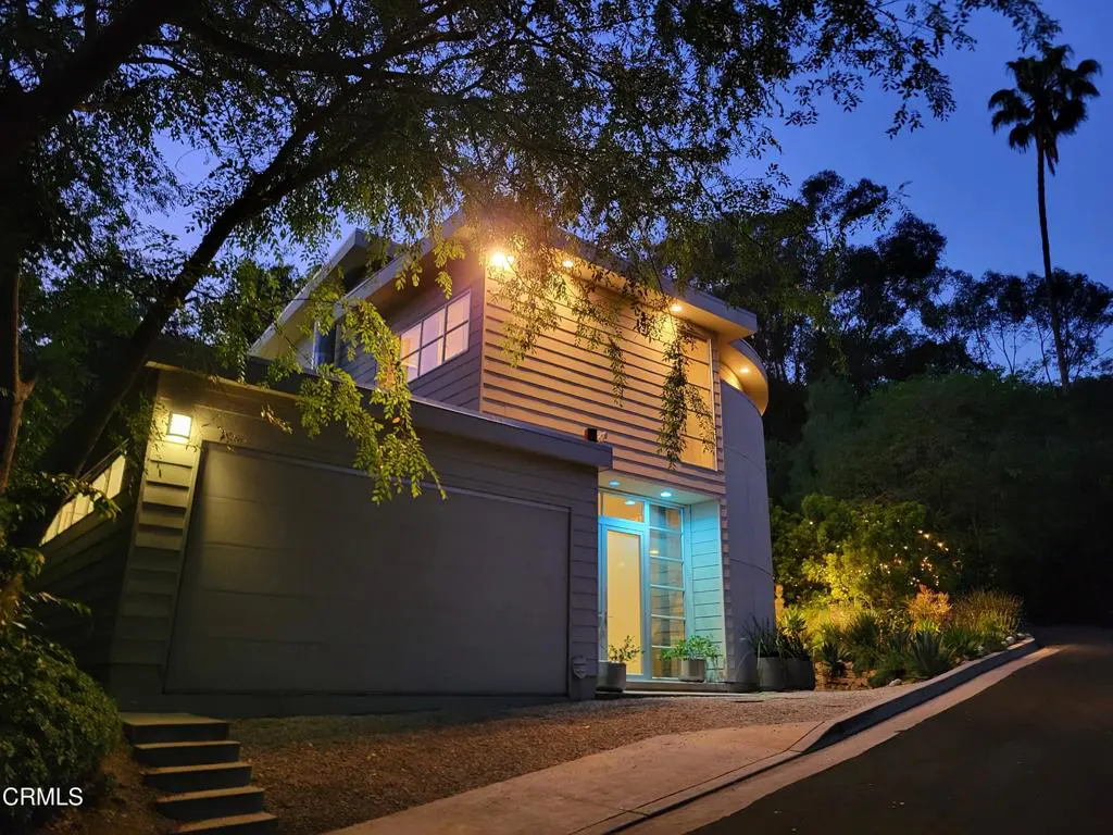 Exterior of a modern two-story home with a gray garage door and light wood siding at dusk.