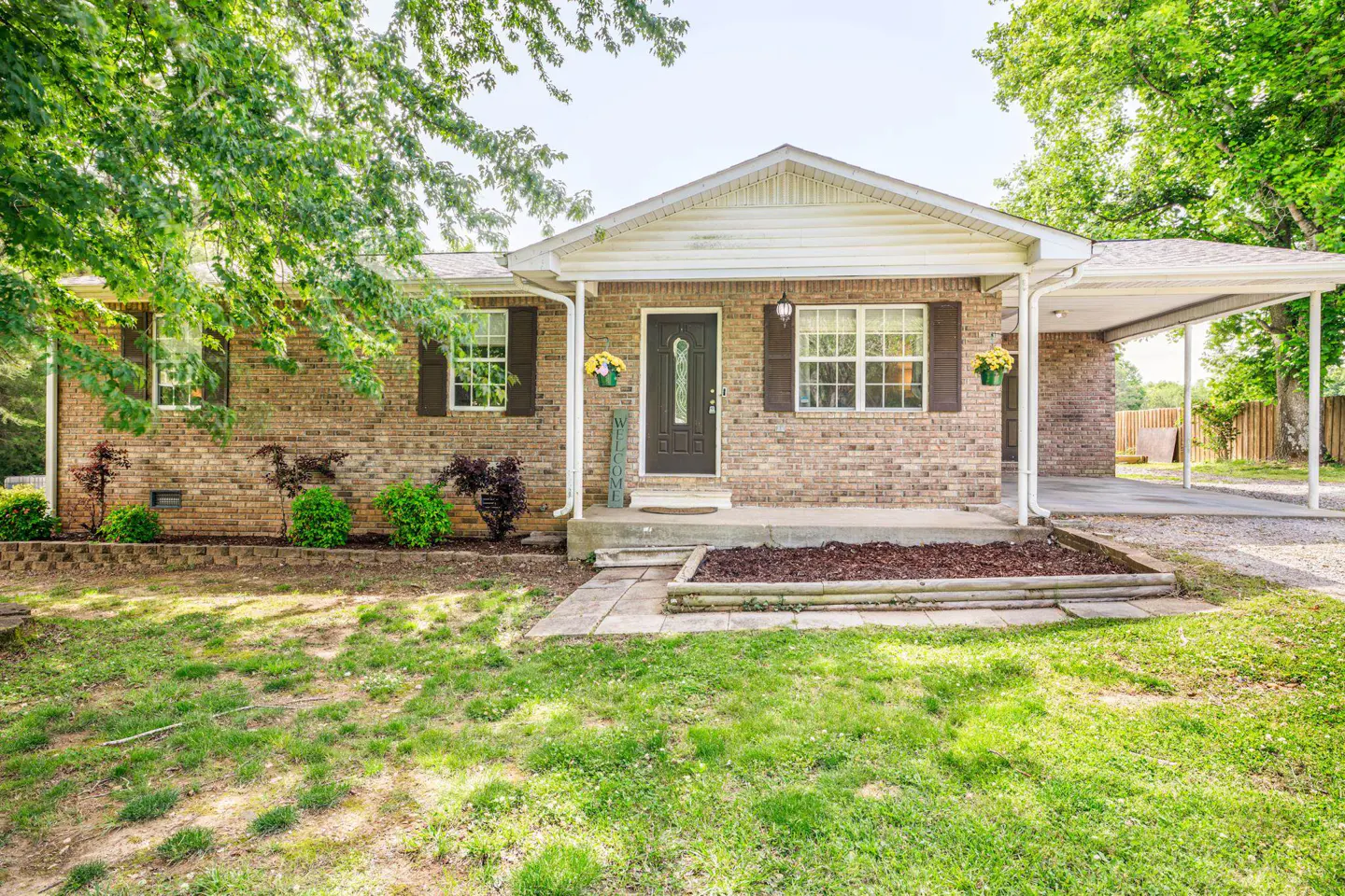 Brick house with a black front door, brown shutters, and a carport on a sunny day.