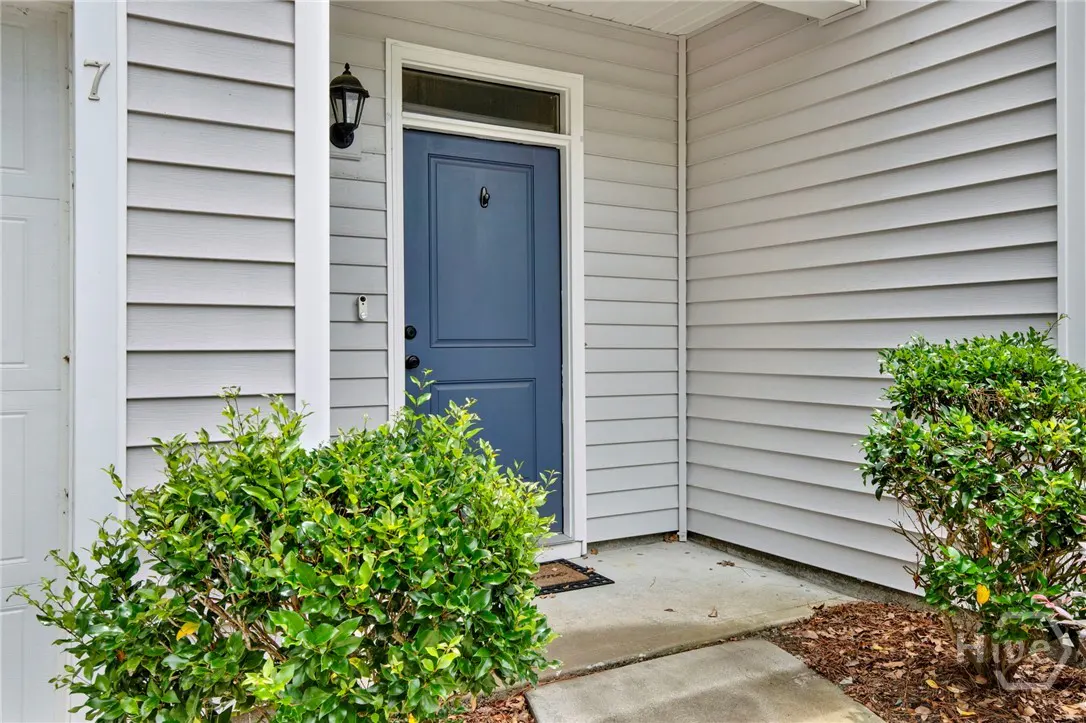 Exterior shot of a home with gray siding, a blue front door with a black knocker, and green bushes.