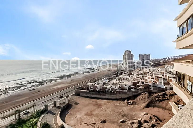 High-angle view of a coastal city with a sandy beach, ocean, and modern buildings under a clear blue sky.