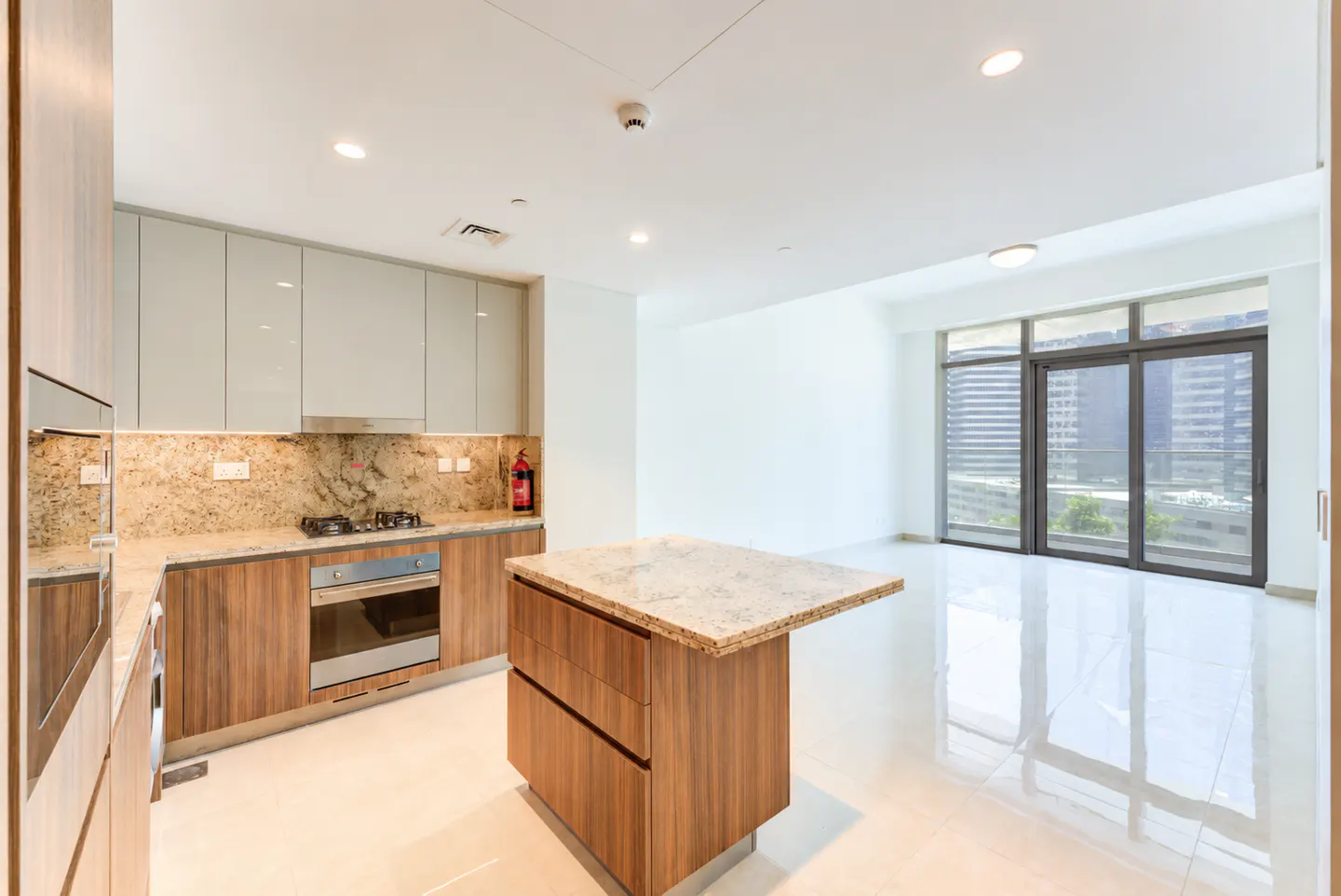 A modern kitchen with wood cabinets, granite countertops, and a central island. Large windows offer a city view.
