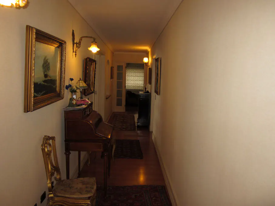 Hallway with beige walls, wood floors, and rugs. A desk, chair, and paintings decorate the left wall.