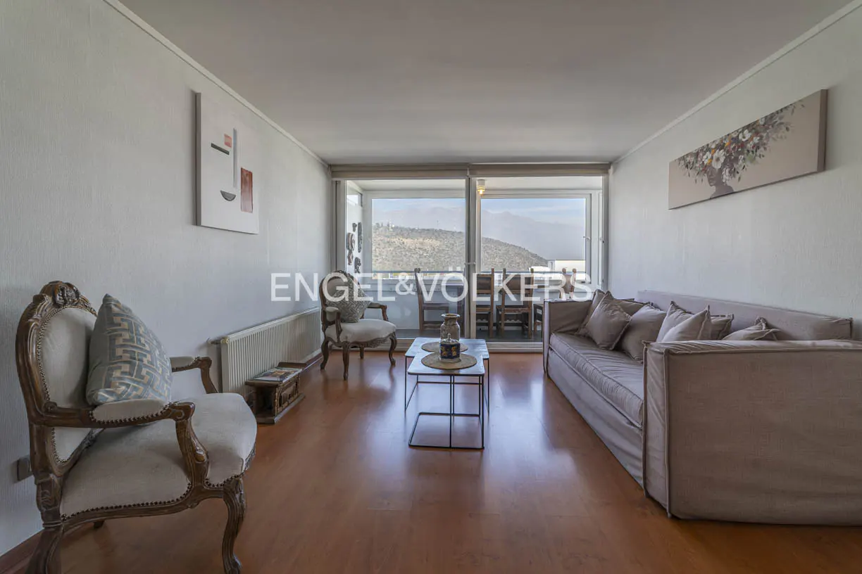 A living room with a beige sofa, two chairs, a coffee table, and a balcony with a mountain view.