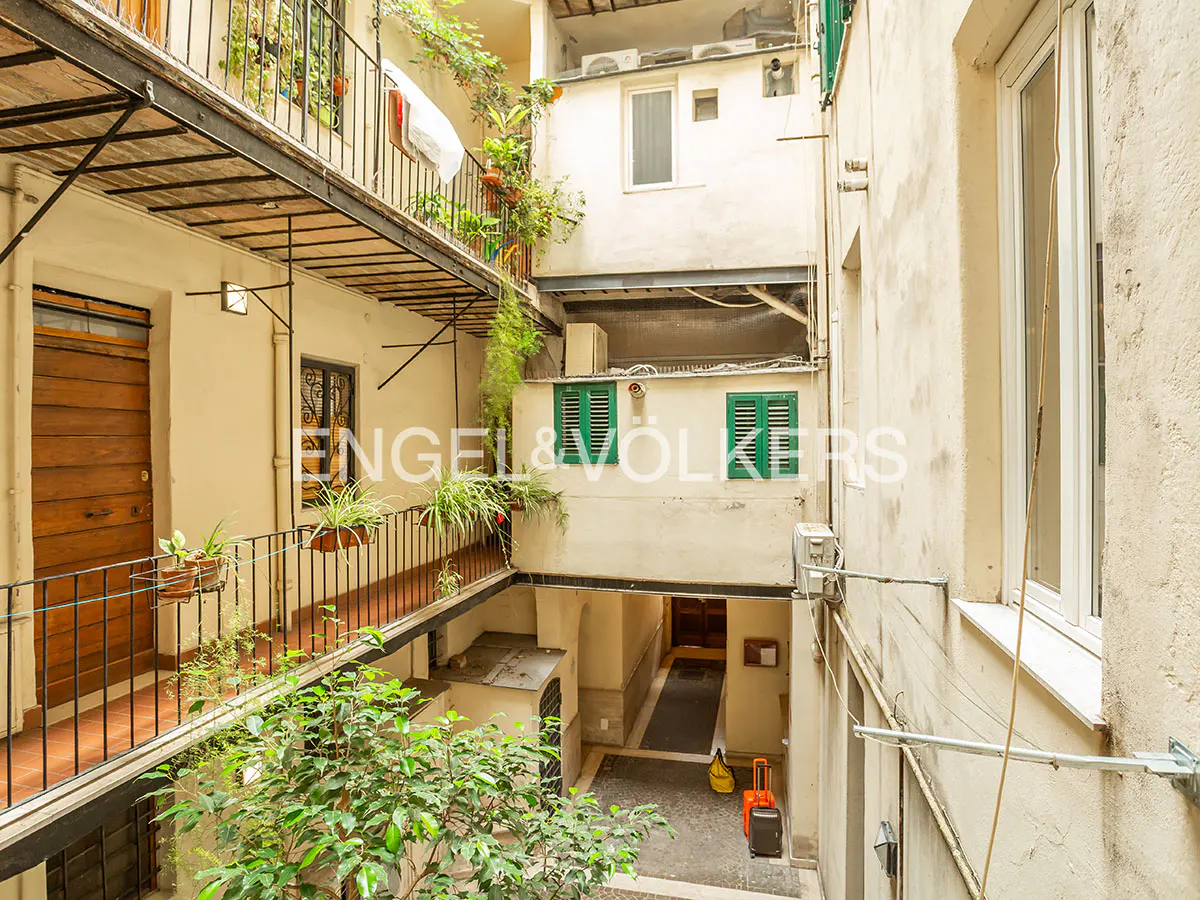 Courtyard view of a multi-story building with balconies, plants, and an Engel & Völkers logo. Suitcases are visible on the ground floor.