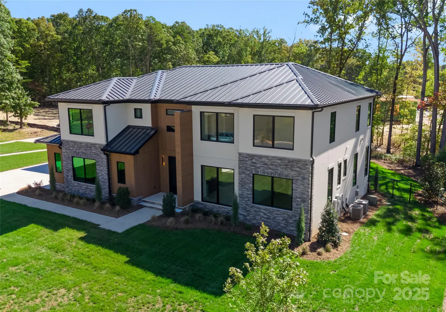 Two-story house with gray metal roof, white stucco, stone, and wood facade, surrounded by green lawn and trees.