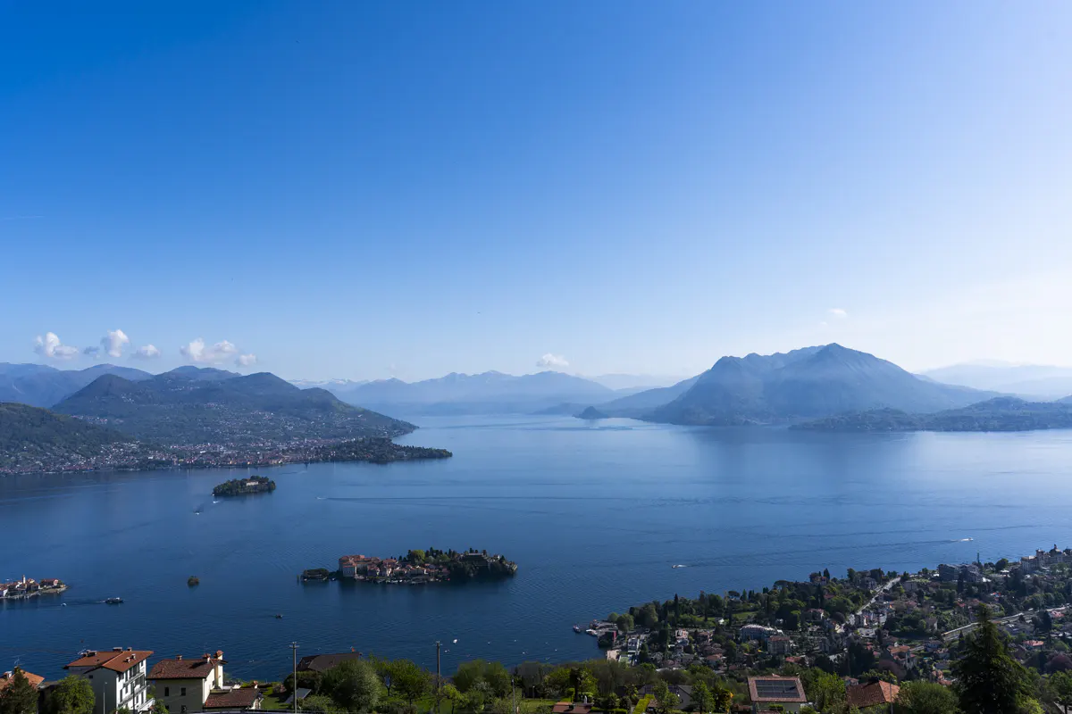 Scenic view of Lake Maggiore, Italy, under a clear blue sky. Mountains surround the lake, with islands and towns visible along the shoreline.