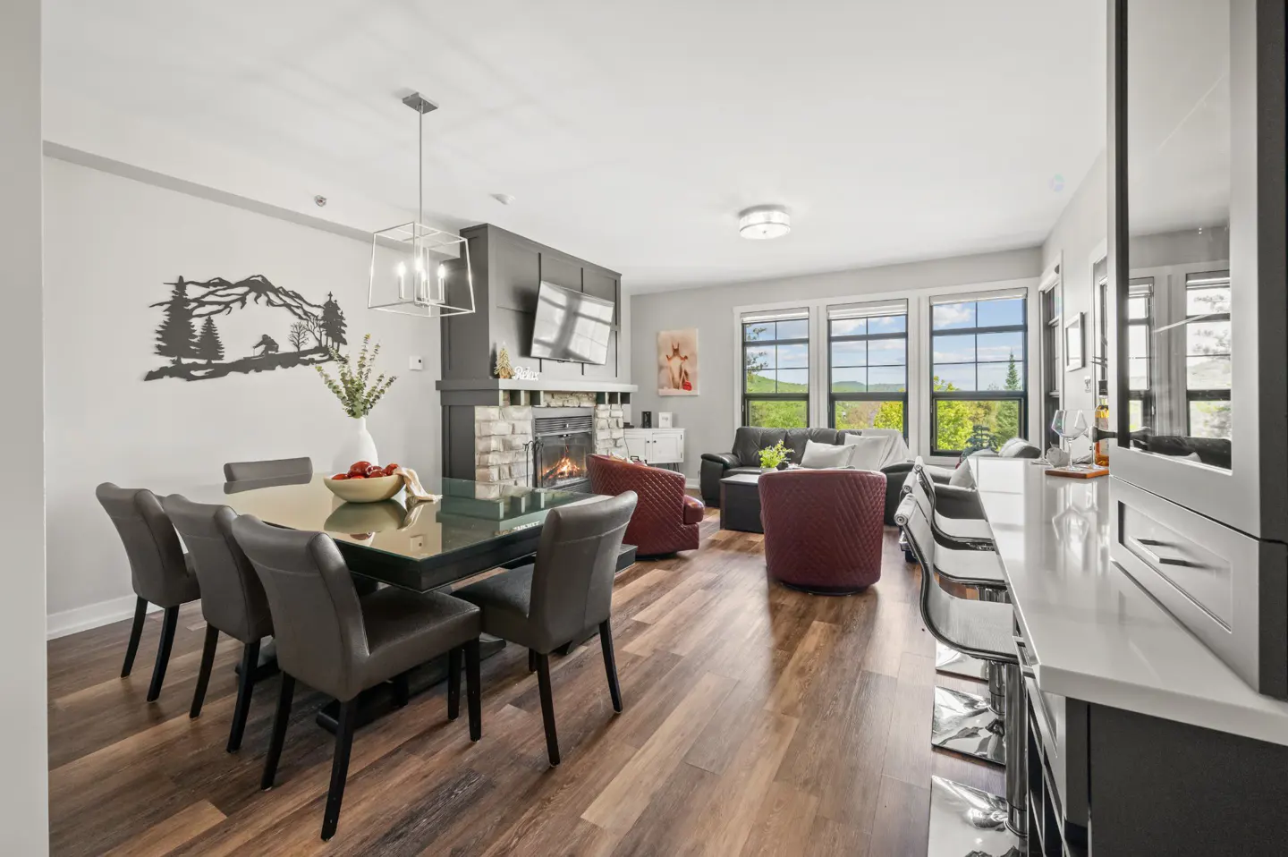 Open-concept living area with a dining table, fireplace, two red armchairs, and a kitchen island with bar stools.