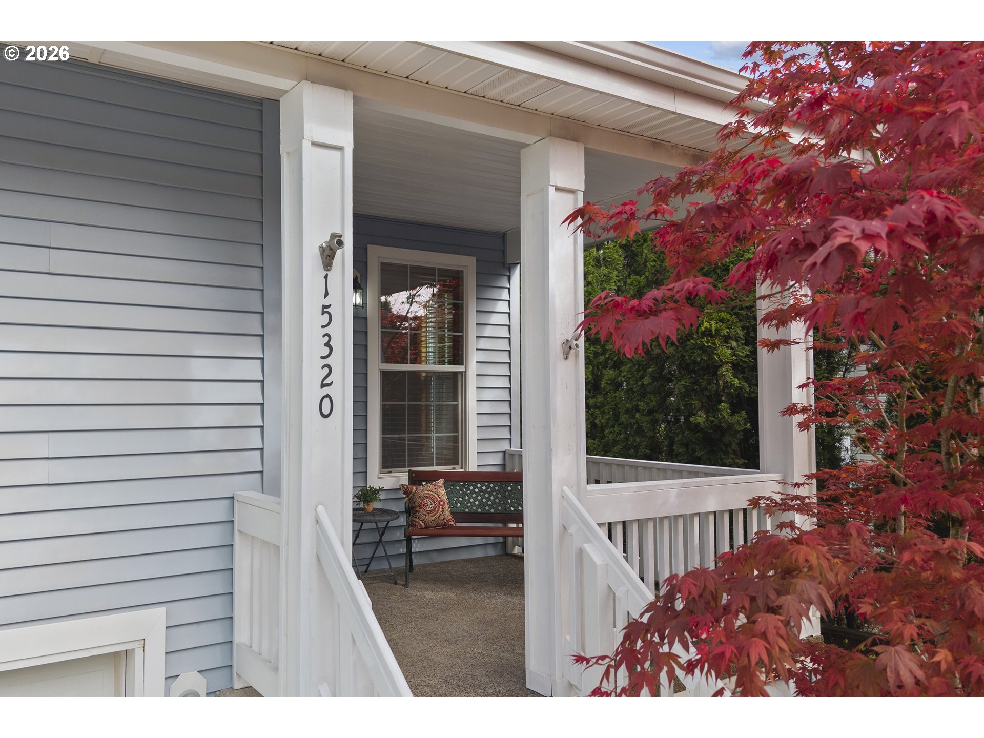 Light blue house porch with white columns, house number 15320, a bench, and a vibrant red Japanese maple tree.