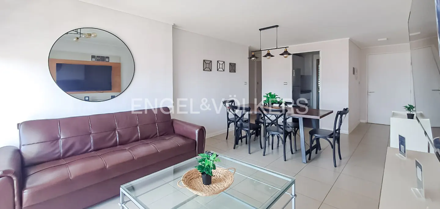 Living room with a brown sofa, glass coffee table, dining table with black chairs, and a round mirror on the wall.